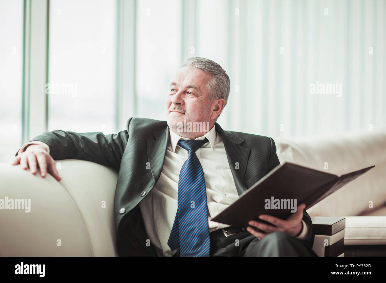 Erfolgreicher Geschäftsmann erwägt, einen neuen Vertrag auf dem Sofa sitzen im eigenen Büro Stockfoto