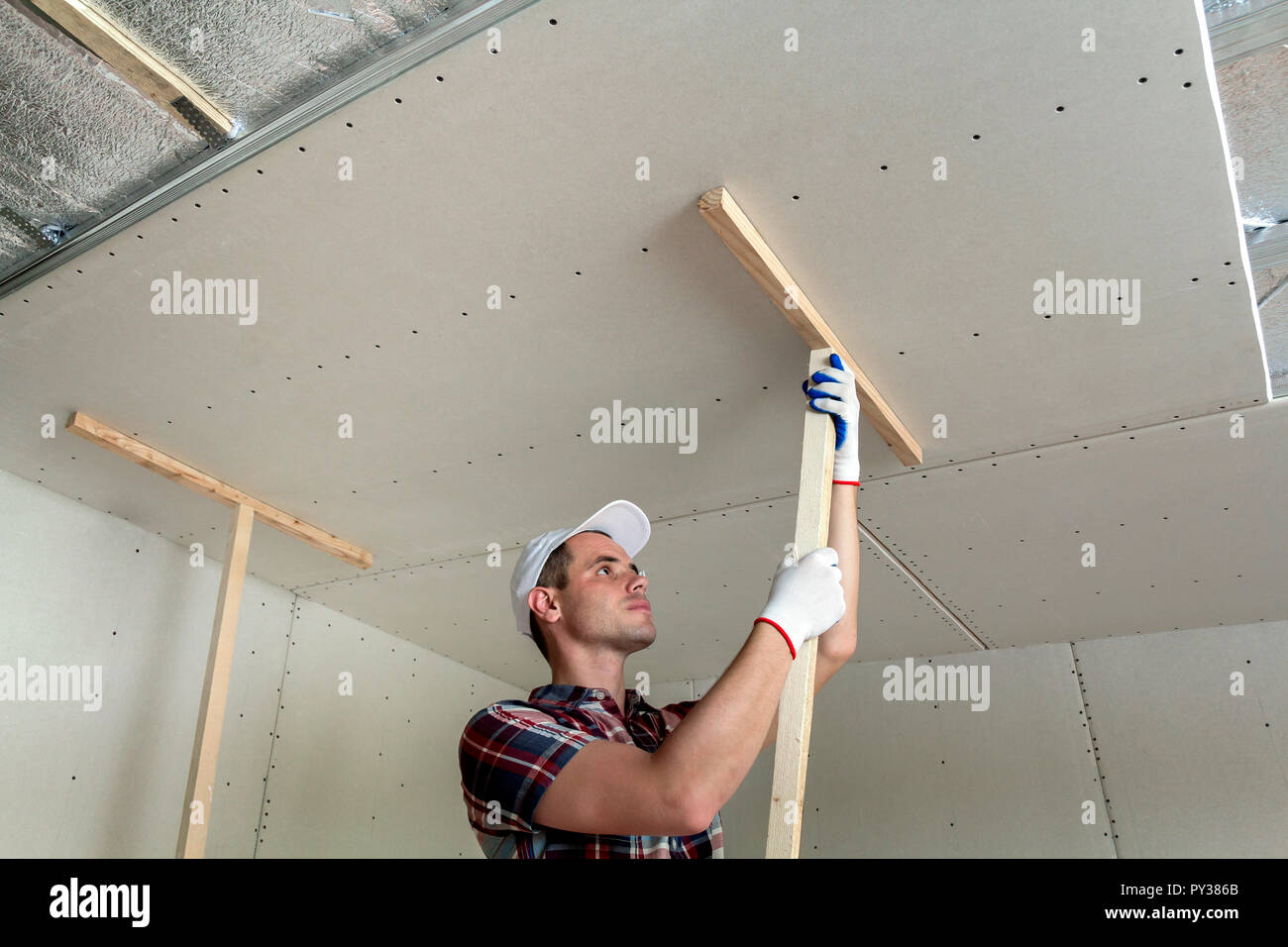 Junge Arbeitnehmer in den Schutz der Arbeit Handschuhe zur Festsetzung  Holz- Halter für Trockenbau decke Metallrahmen mit glänzender  Aluminiumfolie isoliert ausgesetzt. DIY, Do Stockfotografie - Alamy