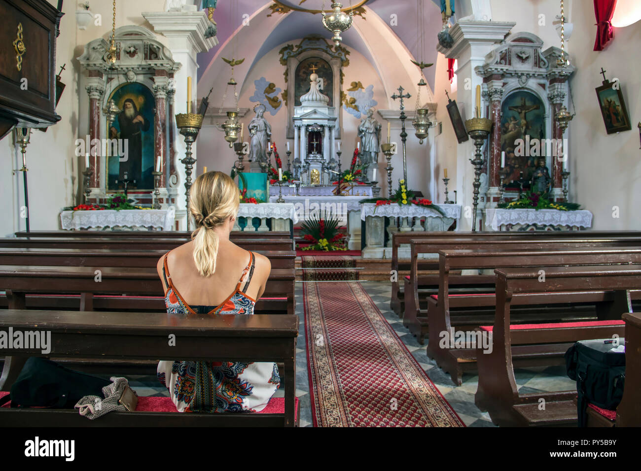 Dobrota, Montenegro, September 2018 - Junge Frau sitzt auf einer Kirchenbank in der Katholischen Kirche St. Matthäus (1670) Stockfoto