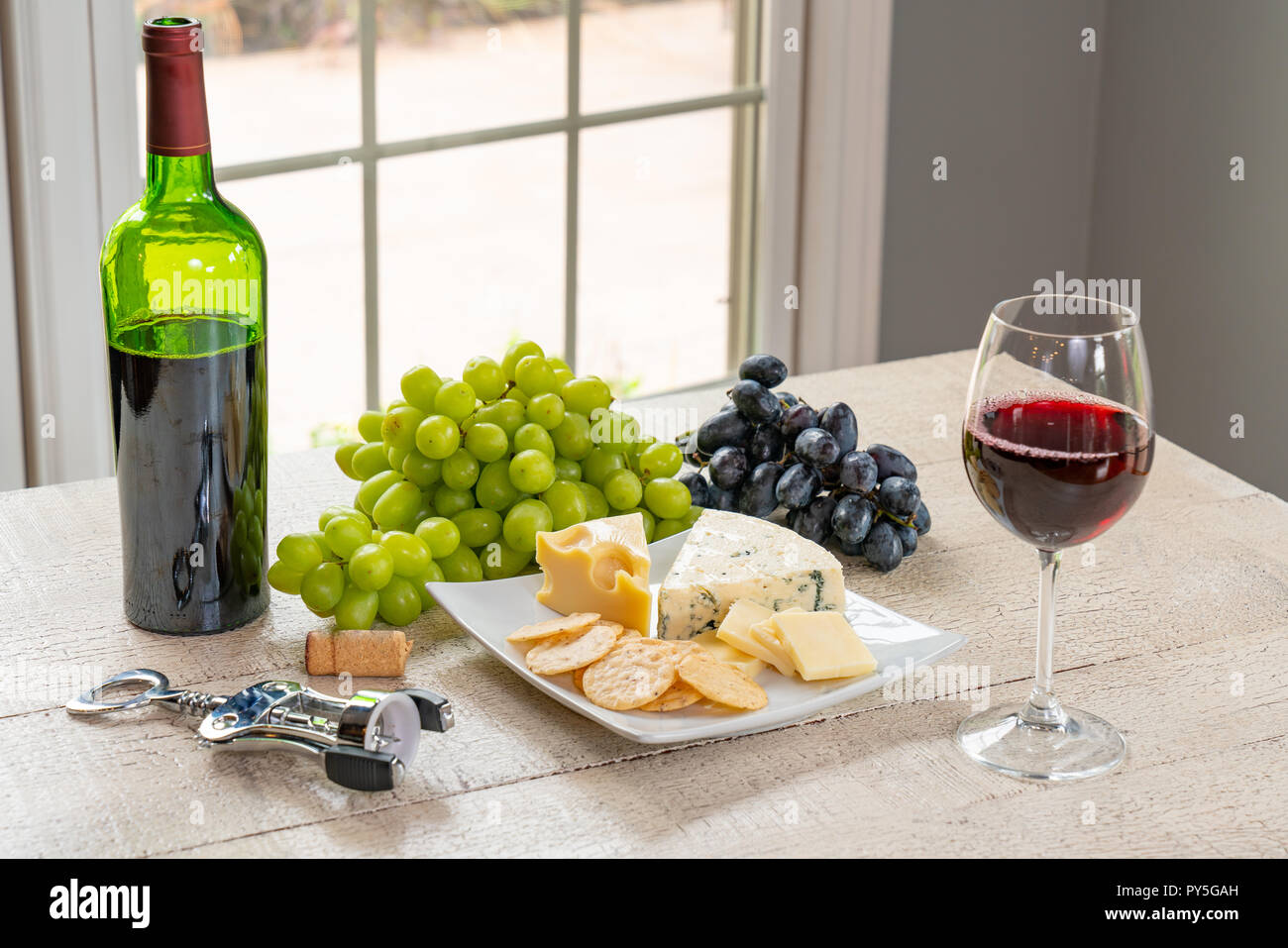 Glas Weißwein mit Flasche Wein, Käse und Trauben Stockfoto