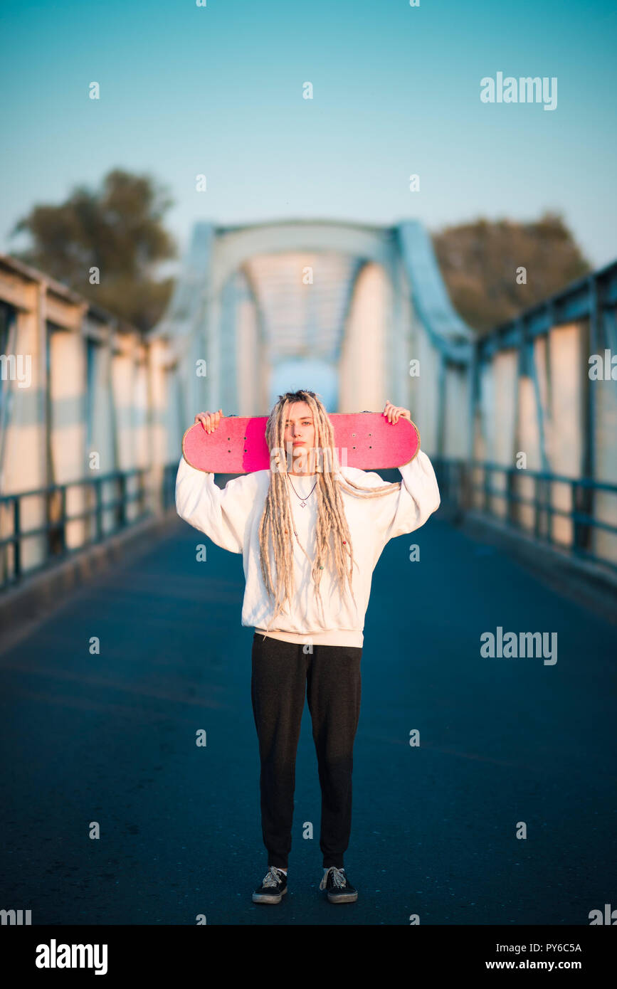 Schöne junge Frau mit rosa Skateboard auf Brücke Stockfoto