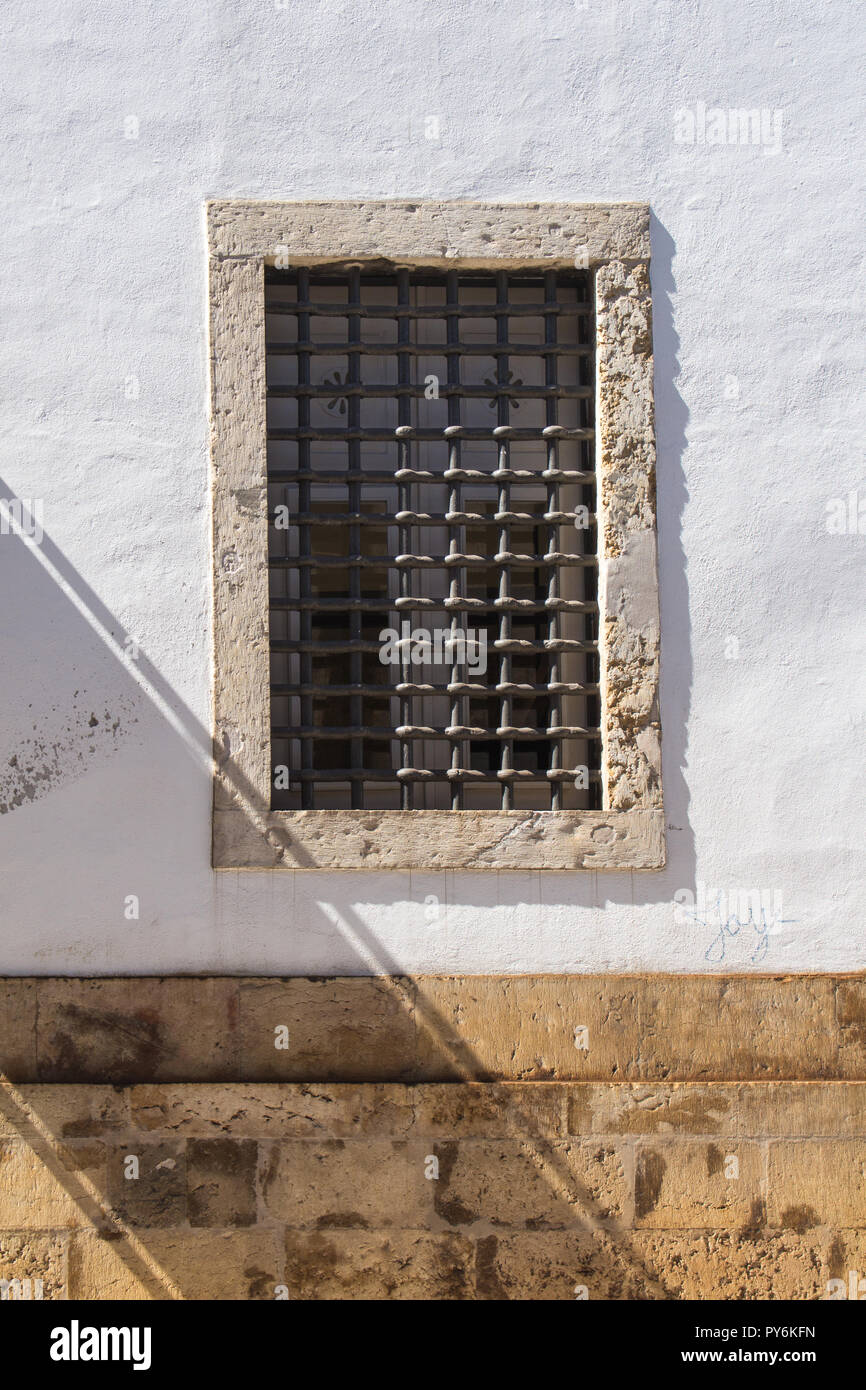 Weiße Fassade eines Gebäudes mit einem großen Fenster mit Gitter und ein Stein. Stein braun Sockel der Wand. Diagonale Schatten. Lissabon, Portugal. Stockfoto