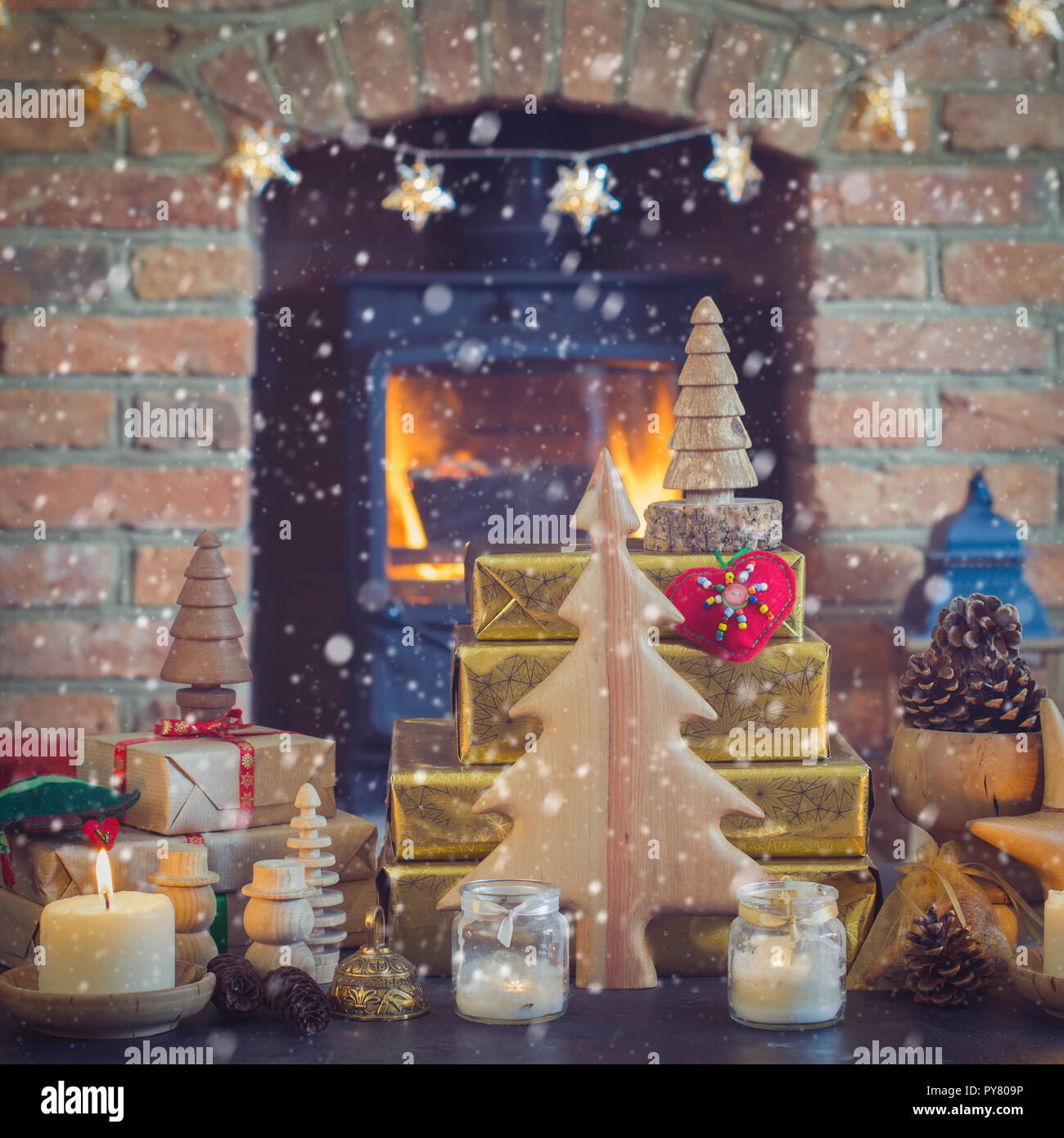 Weihnachten Zusammensetzung, Tannenzapfen in Weidenkorb, Holz- Ornamente, Kerzenlicht mit Fell Äste auf dem Tisch vor einem Kamin Kaminofen Stockfoto
