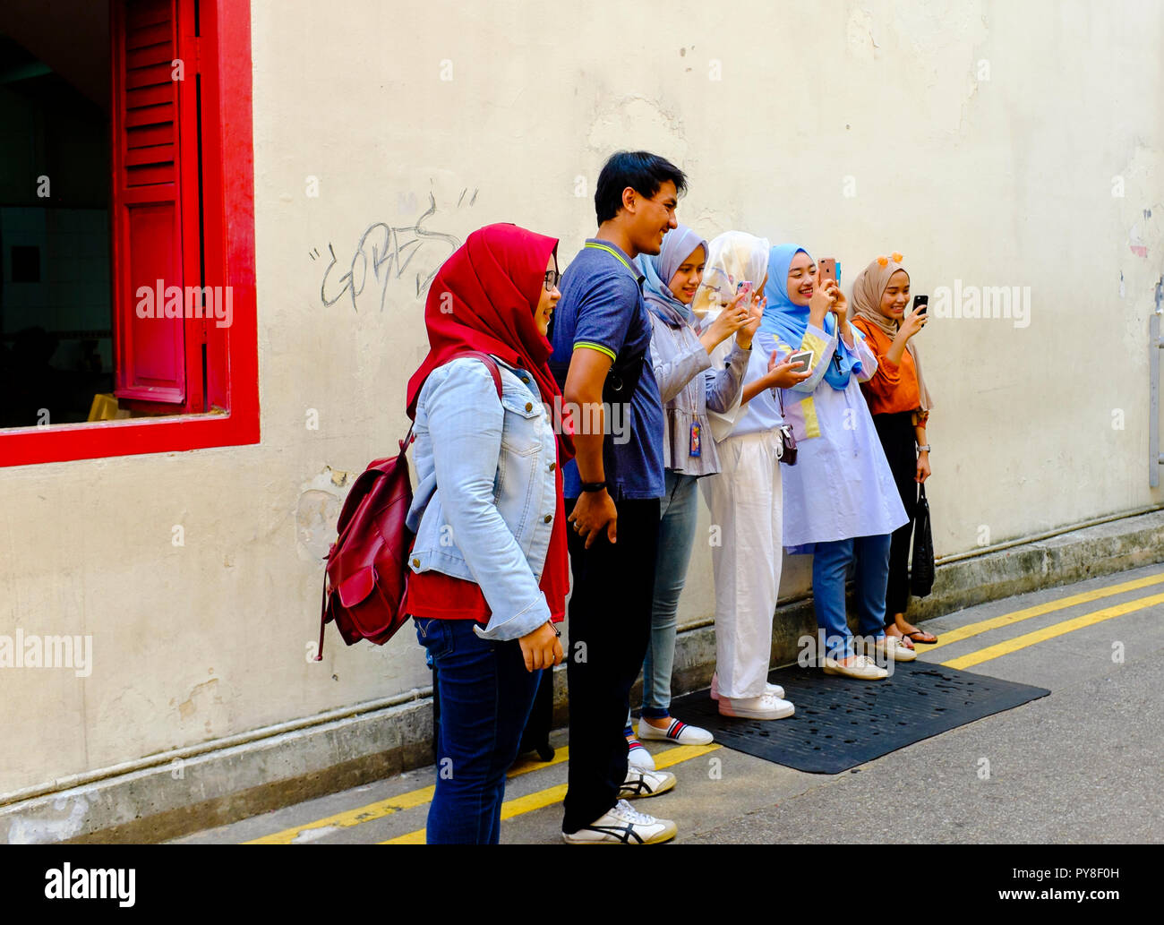 Gruppe von lächelnden jungen Menschen, darunter auch muslimische Mädchen, die hijabs über Telefone auf der Straße in Singapur Stockfoto
