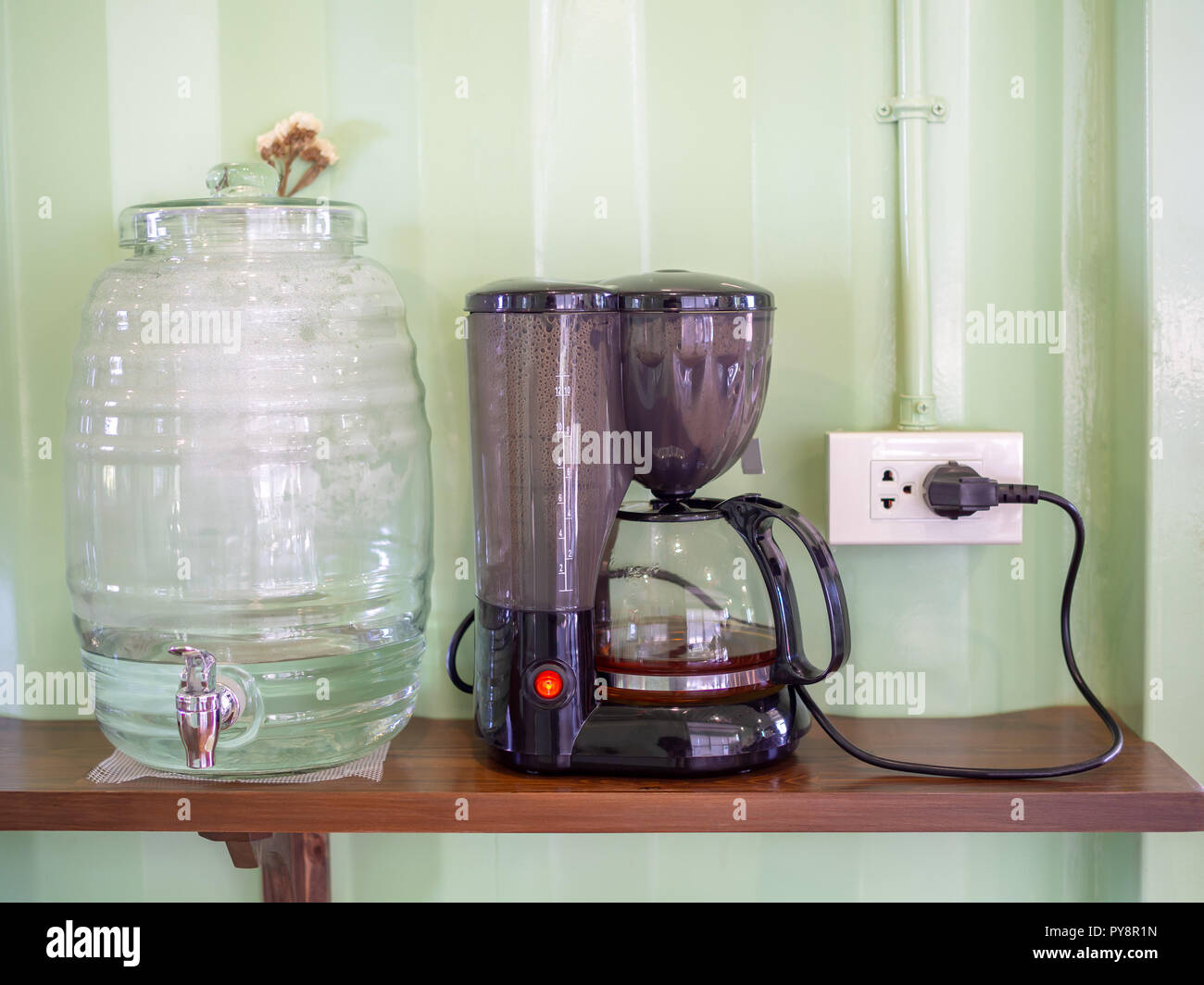 Kühler Flasche und Wasserkocher mit Stecker auf Holzregal auf hellgrün Behälterwand Hintergrund im Cafe. Stockfoto