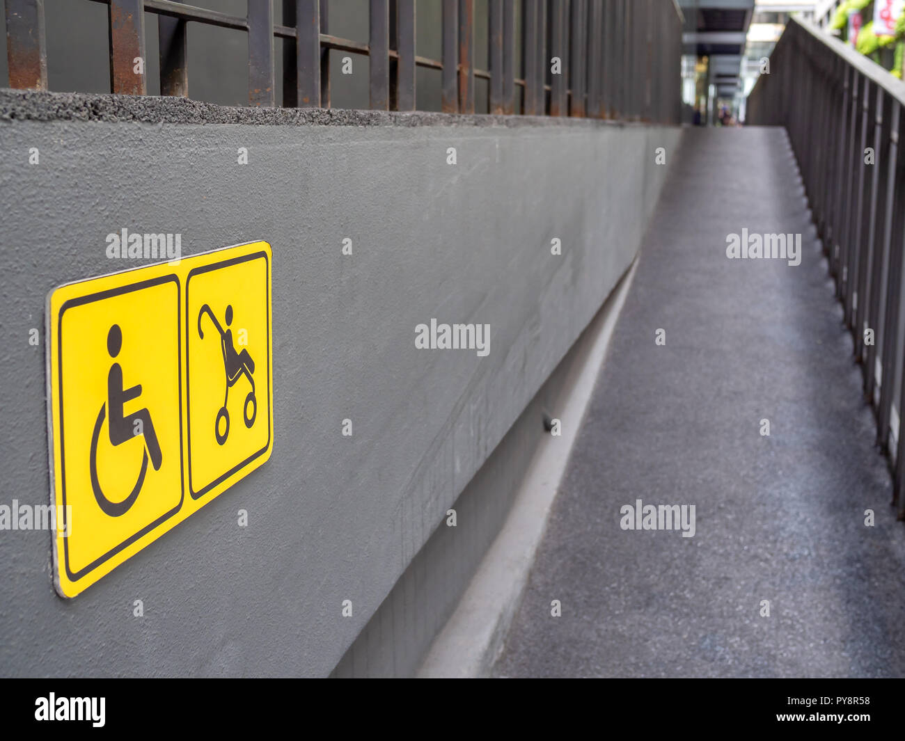 Rollstuhl und Kinderwagen gelbes Schild und an der Wand und Rampe am Gebäude Hintergrund. Stockfoto