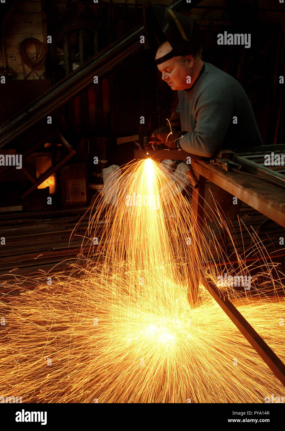 Der Metallarbeiter erzeugt in seiner Werkstatt einen hereinbrausenden Funkenregen Als er in seiner Werkstatt in Schottland Metallarbeiten fertigt Stockfoto