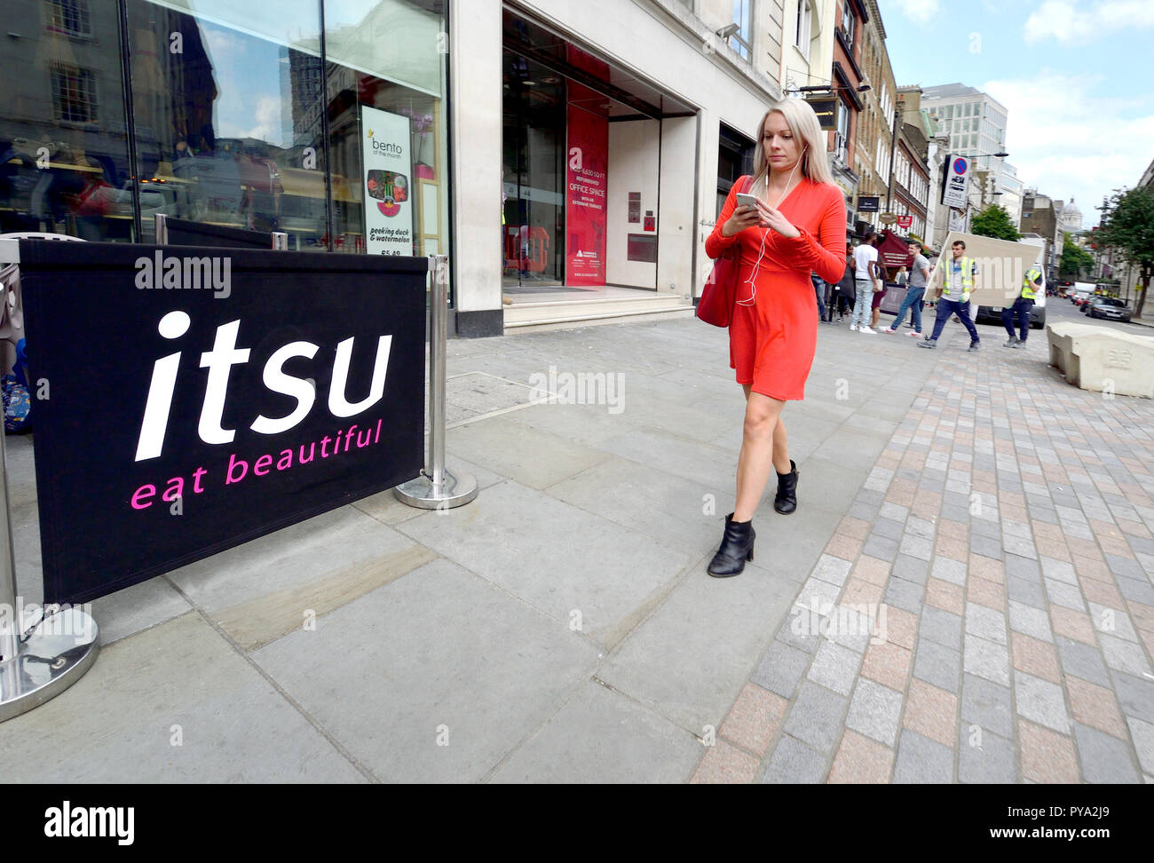 Frau mit Mobiltelefon wandern vorbei an einem Zweig der Itsu (Asiatische fast food) im Zentrum von London, England, UK. Stockfoto