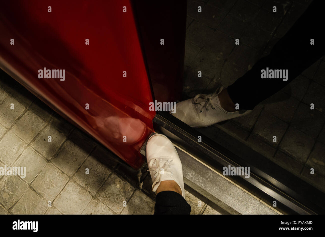 Den Fuß einer Frau mit weißen Schuhen schauen von oben mit der Reflexion von sich selbst in einem schwarzen Spiegel mit einem roten Struktur, Reflexion von 3 weiße Schuhe Stockfoto