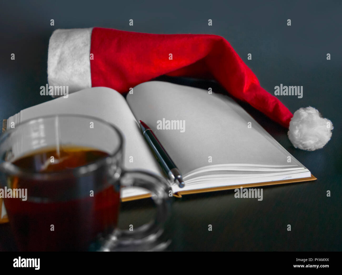 Leer Notebook, schwarze Kugelschreiber, der rote Weihnachtsmütze, Tasse Tee auf einem Holztisch. Beschlüsse des neuen Jahres. Ziele zu setzen, immer bereit neue Sie zu werden, Prom Stockfoto
