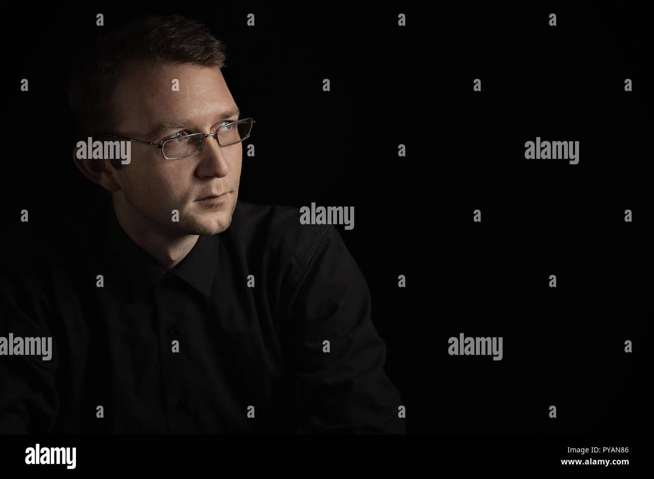 Junger Mann, Nahaufnahme, Porträt, auf schwarzen Hintergrund mit Brille schauen Sie auf die Seite Stockfoto