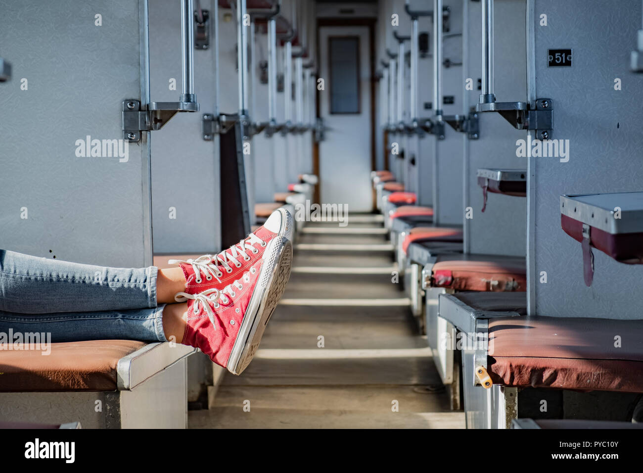 Frau Beine in Rote Tennisschuhe in einem Vintage leerer Zug Auto. Weibliche in Canvas Schuhe ruht auf Sitze einer alten sowjetischen Wirtschaft klasse Schlitten Stockfoto