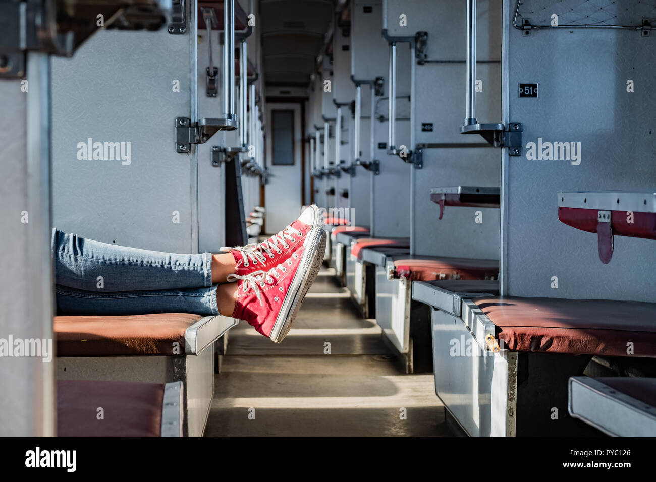 Frau Beine in Rote Tennisschuhe in einem Vintage leerer Zug Auto. Weibliche in Canvas Schuhe ruht auf Sitze einer alten sowjetischen Wirtschaft klasse Schlitten Stockfoto