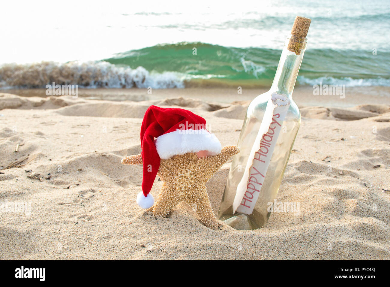 Seesterne mit Santa Mütze im Strand Sand mit happy holiday Message in a Bottle Stockfoto