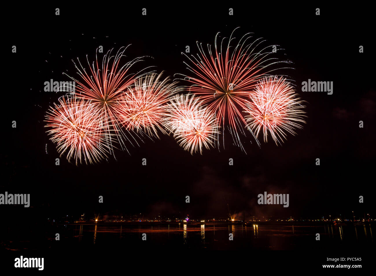 Riesige rote Feuerwerkskörper Raketen Explosionen in dunkler Nacht am See Stockfoto