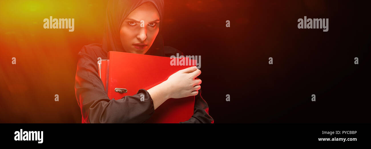 Porträt der Schönen verzweifelte Angst junge muslimische Frau mit schwarzen Hijab holding Ordner als geheim halten Konzept auf schwarzem Hintergrund Angst Stockfoto