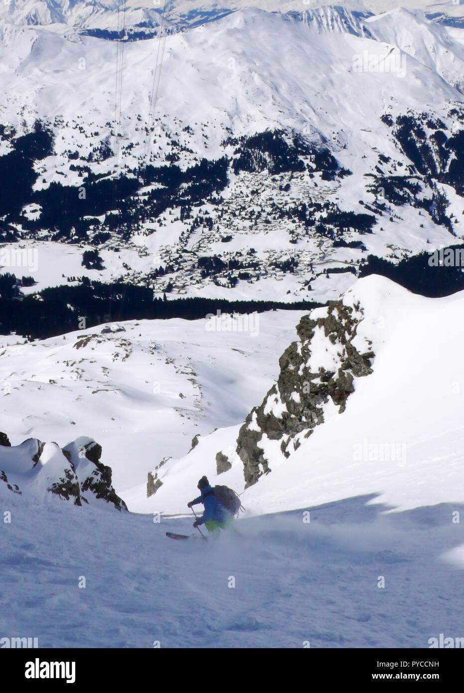 Extreme Skifahrer Skifahren in einem schmalen Schneecouloir mit Blick auf alpinen Dörfer weit unten im Tal in der Schweiz Stockfoto