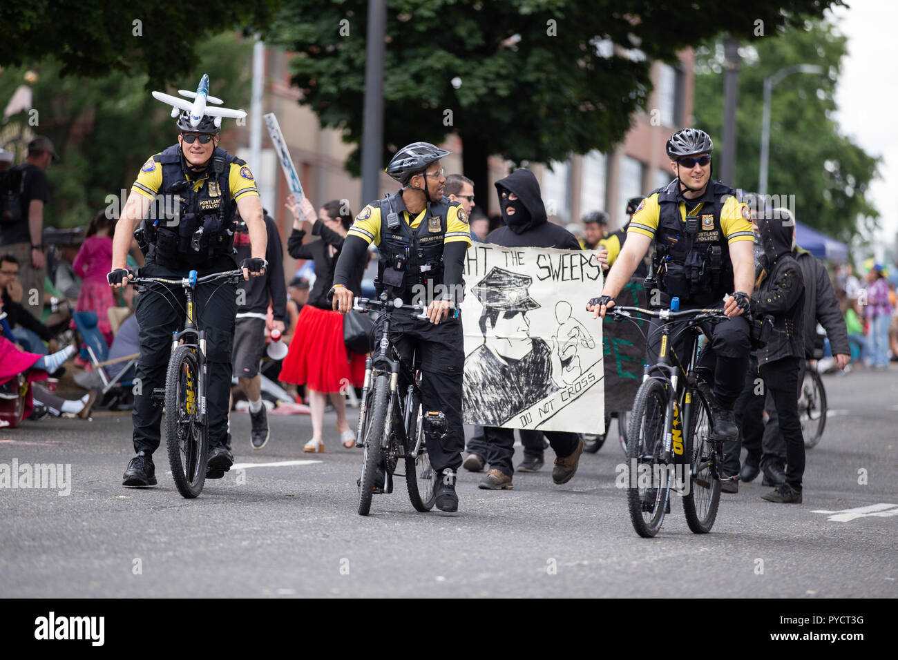 Portland, OR/USA - 11. Juni 2016: Grand floral Parade. Polizisten auf Fahrräder reiten entlang der Seite anti Cop maskierte Demonstranten. Stockfoto