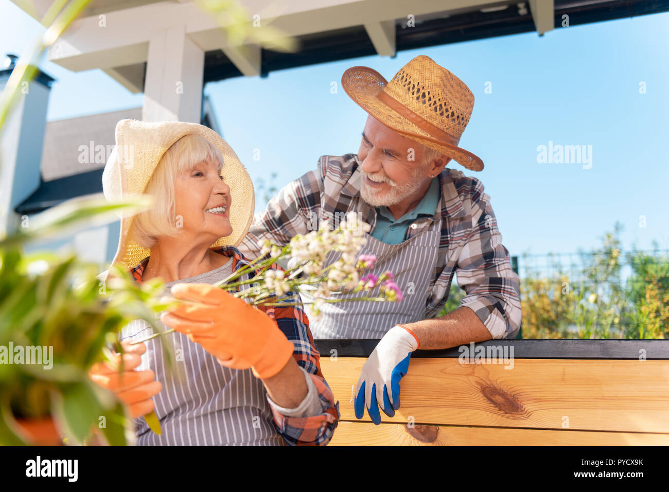 Strahlende ältere Dame mit weißen Blumen auf ihrem stattlichen Mann sucht Stockfoto