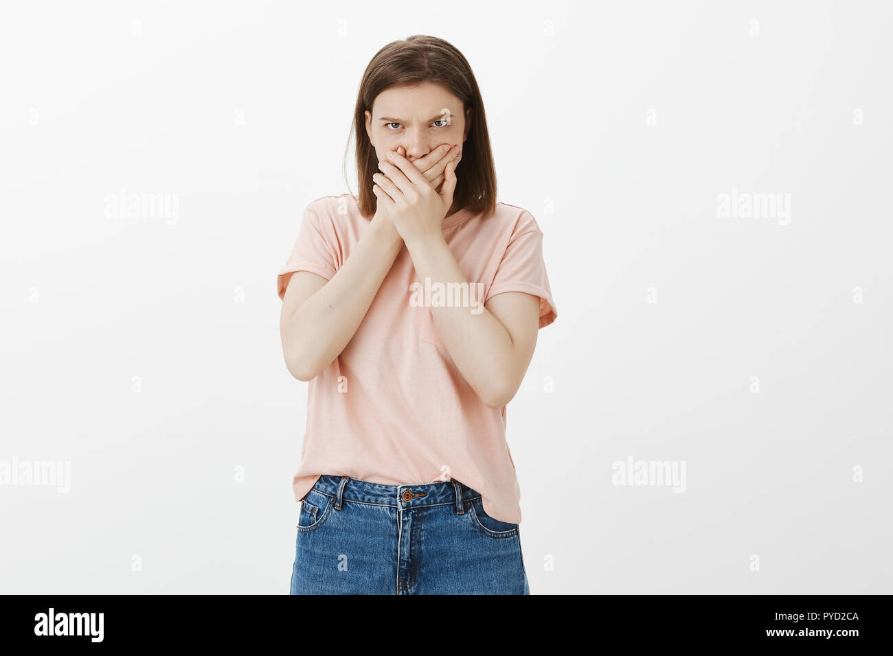 Sie ist nicht gehend zu Wort. Portrait der beleidigten wütende Frau verbleibenden sprachlos, der Mund mit beiden Handflächen, runzelte die Stirn und suchen unter der Stirn mit Hass und Zorn, stehend über graue Wand Stockfoto