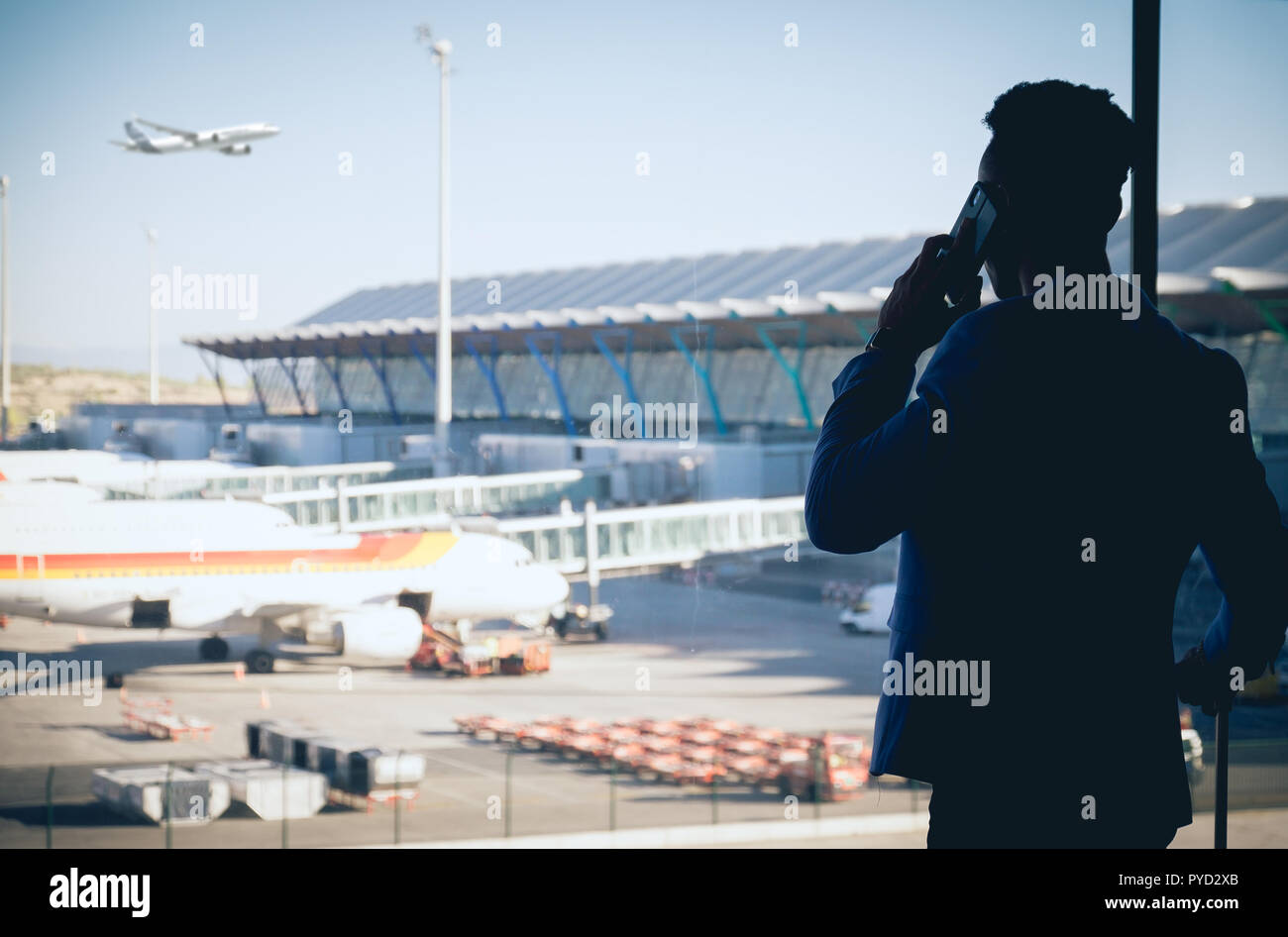 Ein junger und attraktiver Geschäftsmann sucht durch das Fenster in der Flughafen Terminal. Ein Flugzeug fliegt, während andere auf dem Grundstück geparkt werden Stockfoto