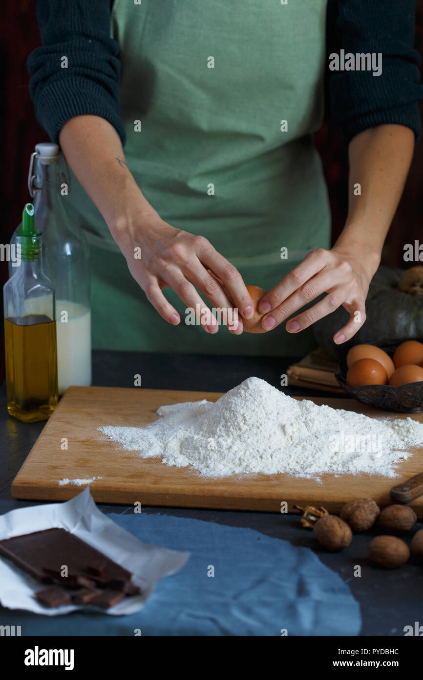 Hände kneten den Teig von Frauen. Der konditor ist ein Ei in das Mehl. Auf dem hölzernen Tisch backen Zutaten. Muttern Mehl Milch Kürbis Stockfoto