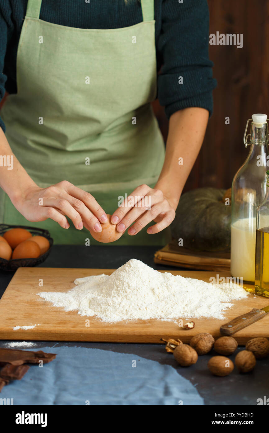 Hände kneten den Teig von Frauen. Der konditor ist ein Ei in das Mehl. Auf dem hölzernen Tisch backen Zutaten. Muttern Mehl Milch Kürbis Stockfoto