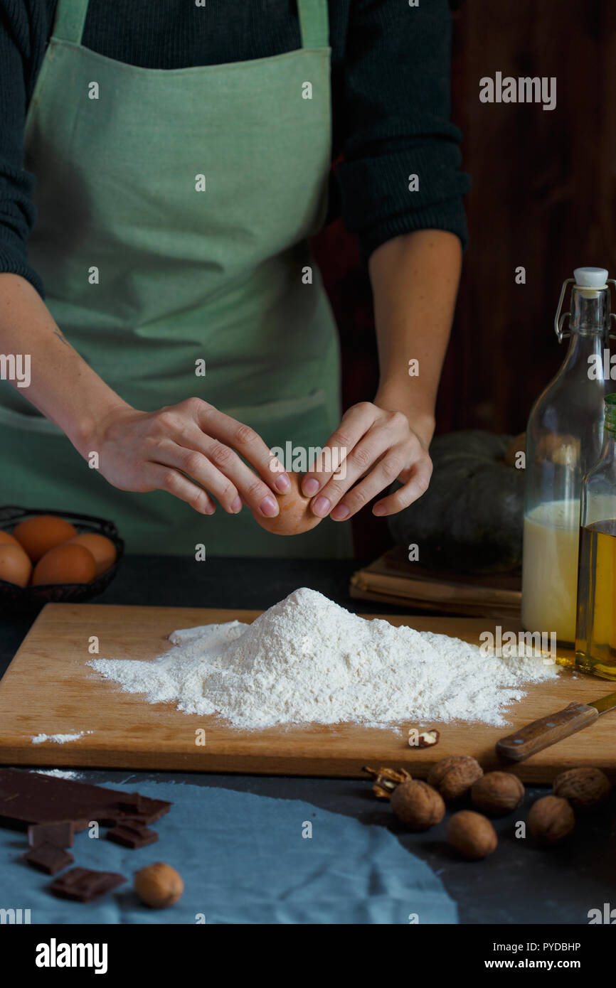 Hände kneten den Teig von Frauen. Der konditor ist ein Ei in das Mehl. Auf dem hölzernen Tisch backen Zutaten. Muttern Mehl Milch Kürbis Stockfoto