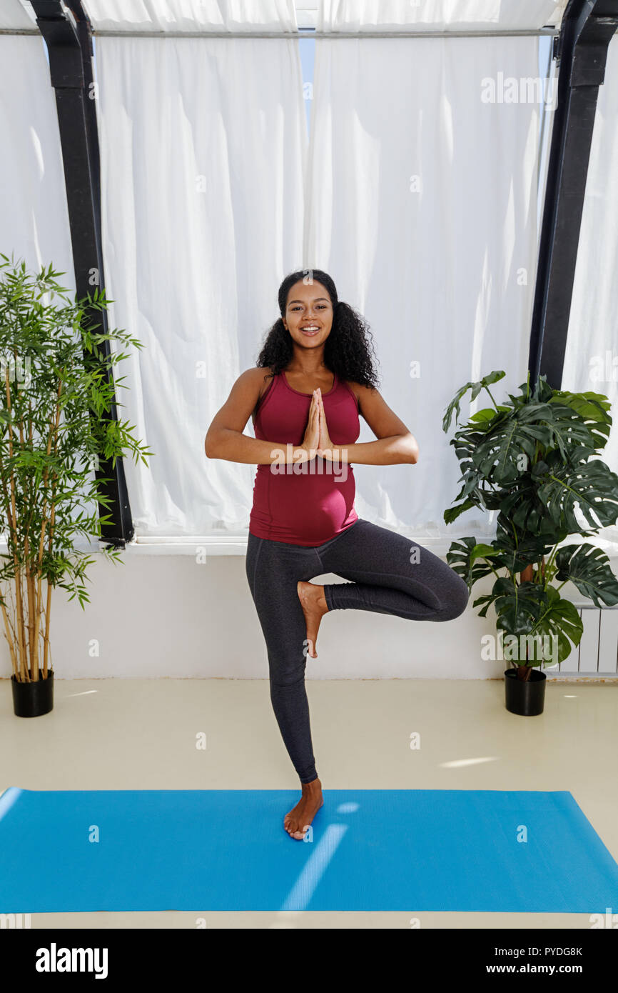 Lächelnd schwangere Frau tun Schwangerschaftsyoga in die baumhaltung Stockfoto
