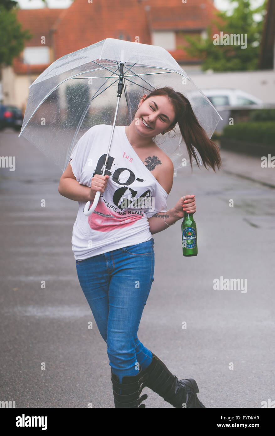 Eine junge Frau mit einem Regenschirm in der Hand tanzt im Regen hält eine Flasche Heineken alkoholfreies Bier Stockfoto