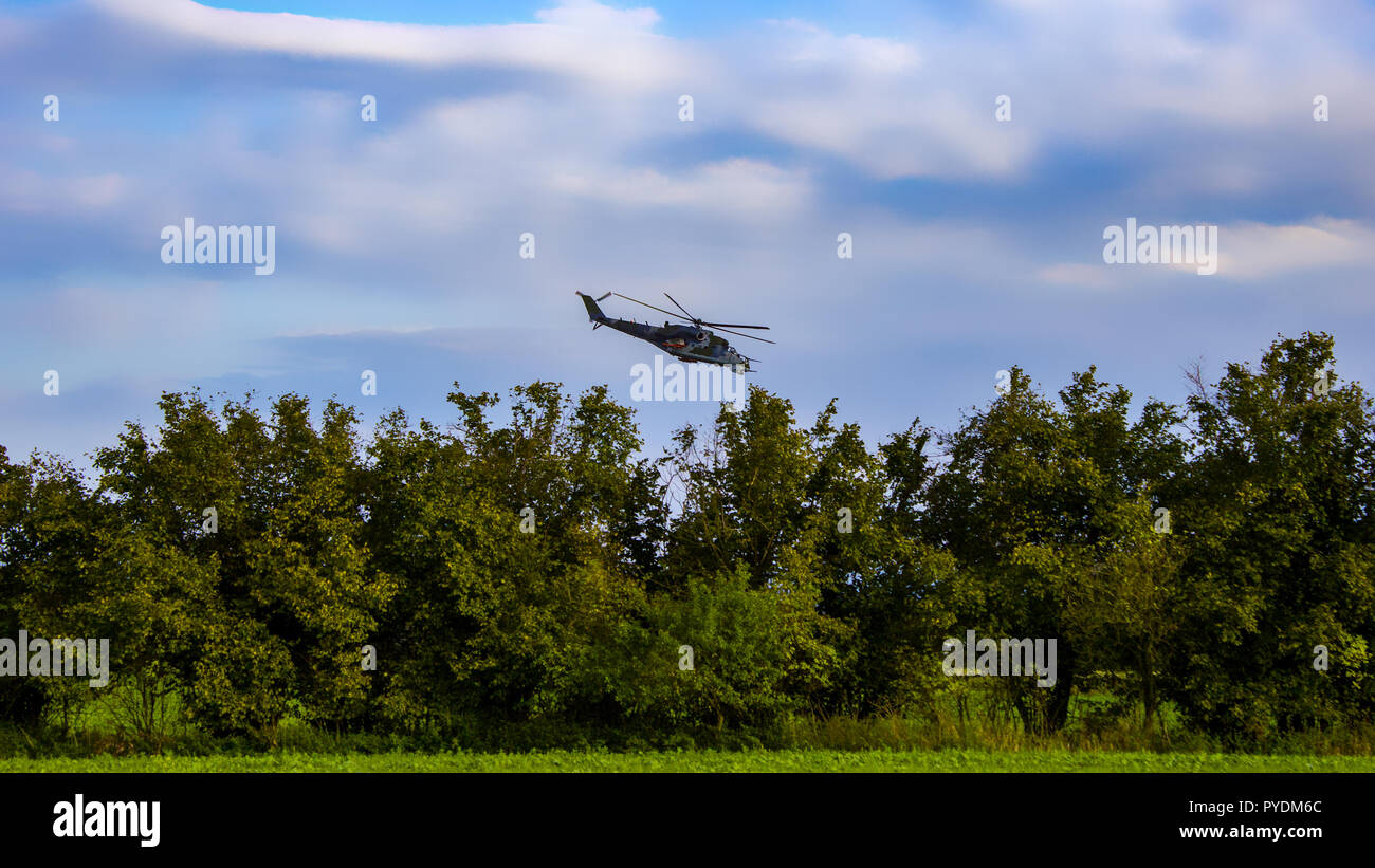 Kampfhubschrauber auf blauer Himmel mit weißen Wolken. Bäume und Bush mit Gras. Stockfoto