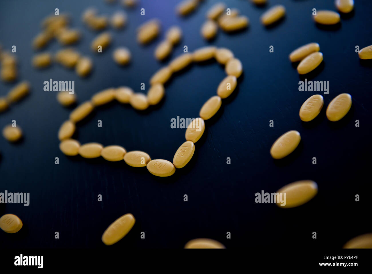 Gelbe Pillen in Form eines Herzens auf den Schwarzen Tisch Stockfoto