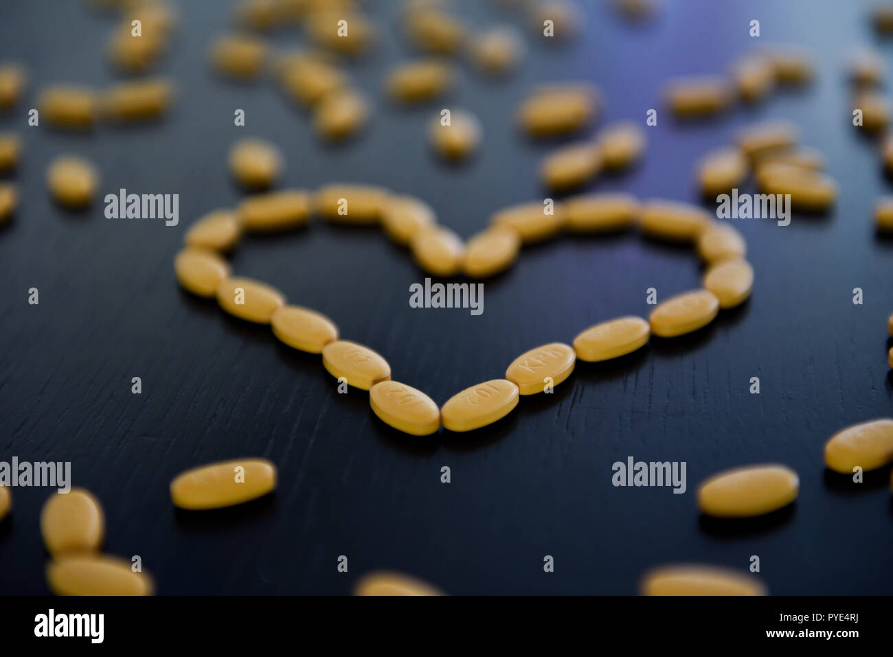 Gelbe Pillen in Form eines Herzens auf den Schwarzen Tisch Stockfoto
