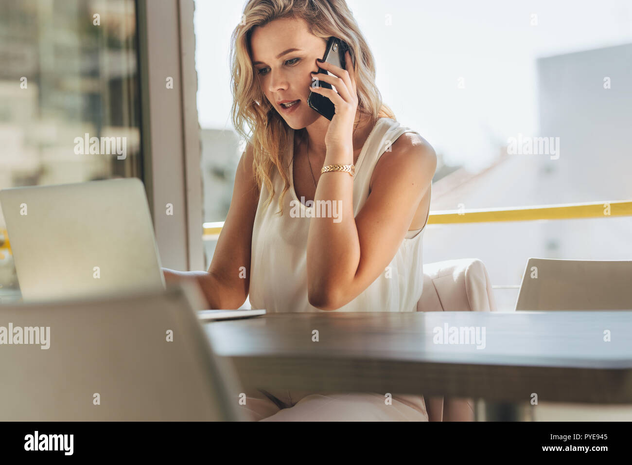 Junge Geschäftsfrau im Café arbeiten. Kaukasische Frau im Cafe sitzen am Laptop auf der Suche und im Gespräch mit Kunden über Smart Phone. Stockfoto