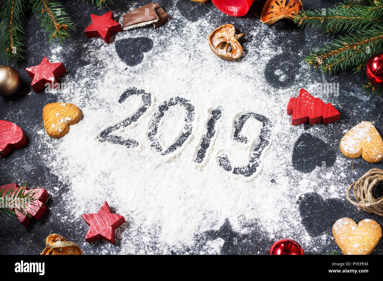 Frohes Neues Jahr 2019 auf Mehl und Weihnachtsschmuck Lebkuchen Cookies auf dunklem Stein Hintergrund geschrieben. Neues Jahr Grußkarte Stockfoto