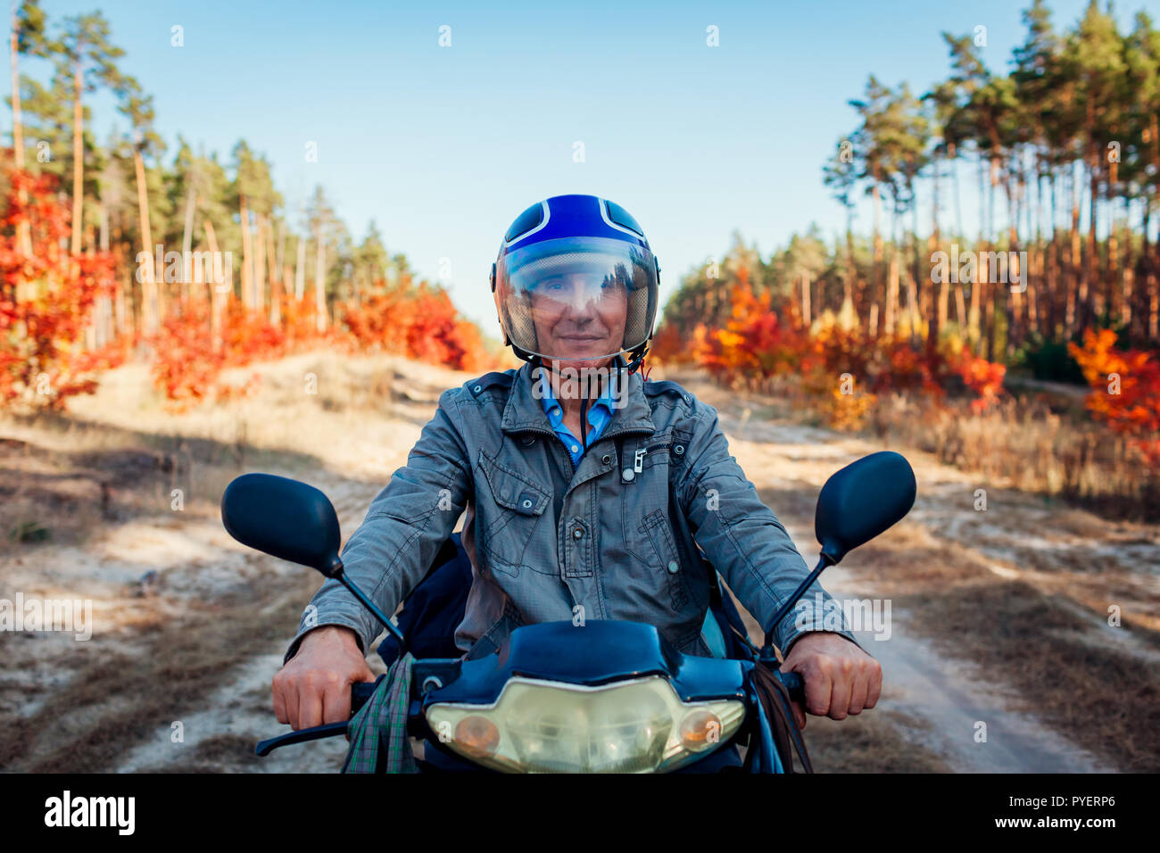 Ältere Menschen reiten Roller auf autumn forest road. Gerne Fahrer in Helm reiten Moped. Stockfoto