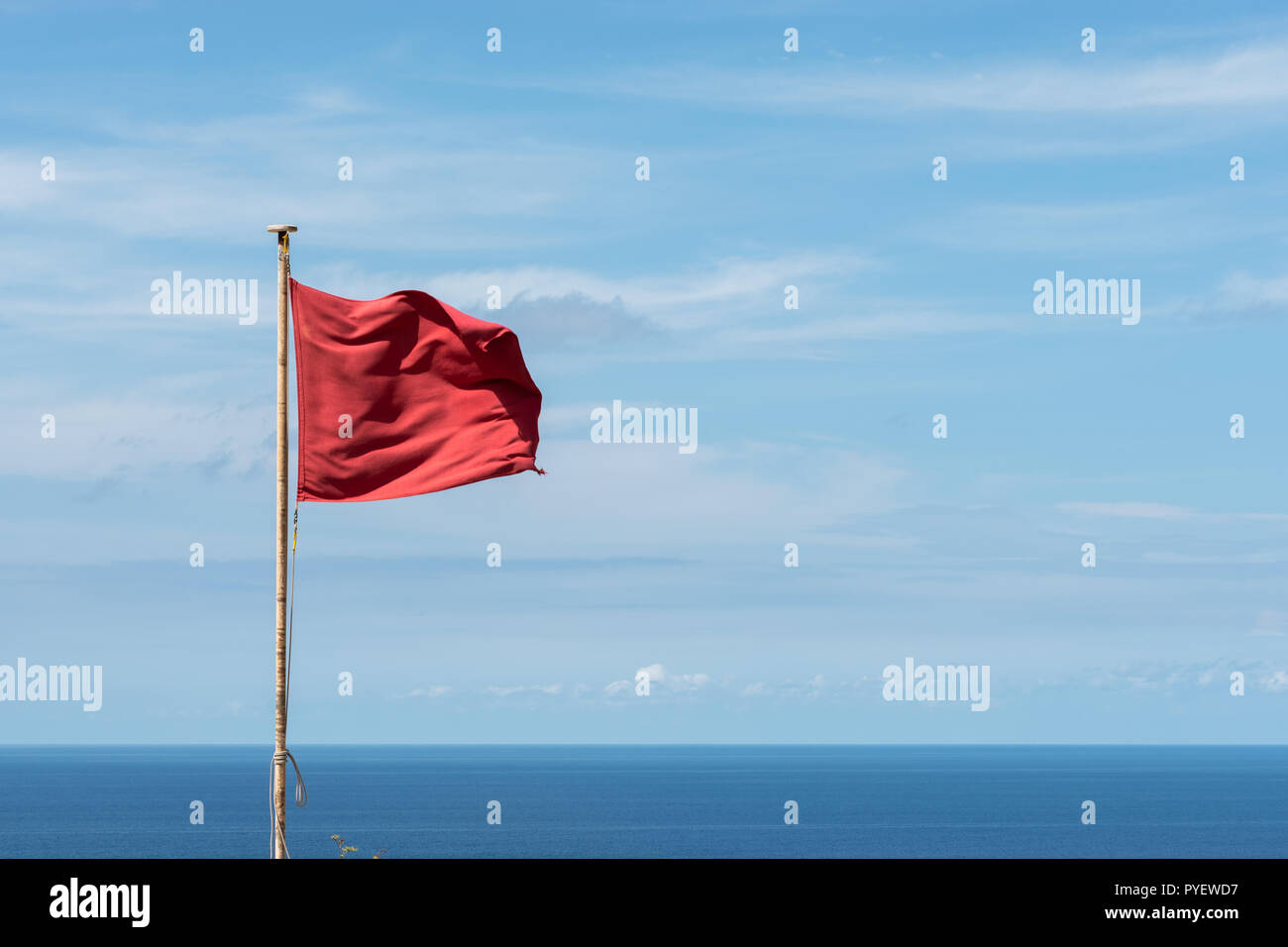 Rote Fahne schwenkten auf einer Stange. Wolken und das Meer im Hintergrund. Horizontale Ansicht Stockfoto