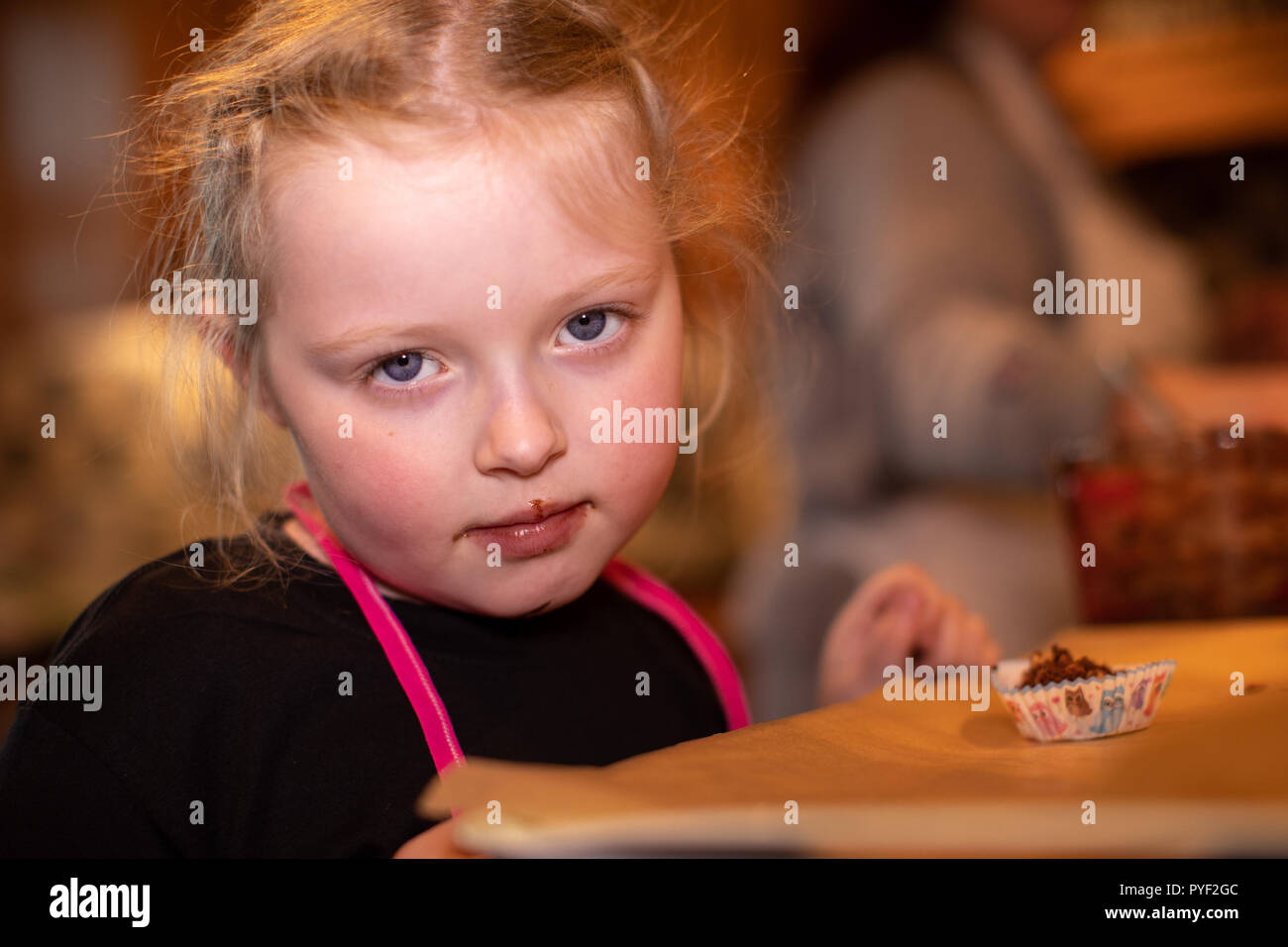 Kleines Mädchen sieht traurig, als Sie versucht ist ein Brötchen, die Sie gerade mit Ihrer Mutter gekocht hat zu essen Stockfoto