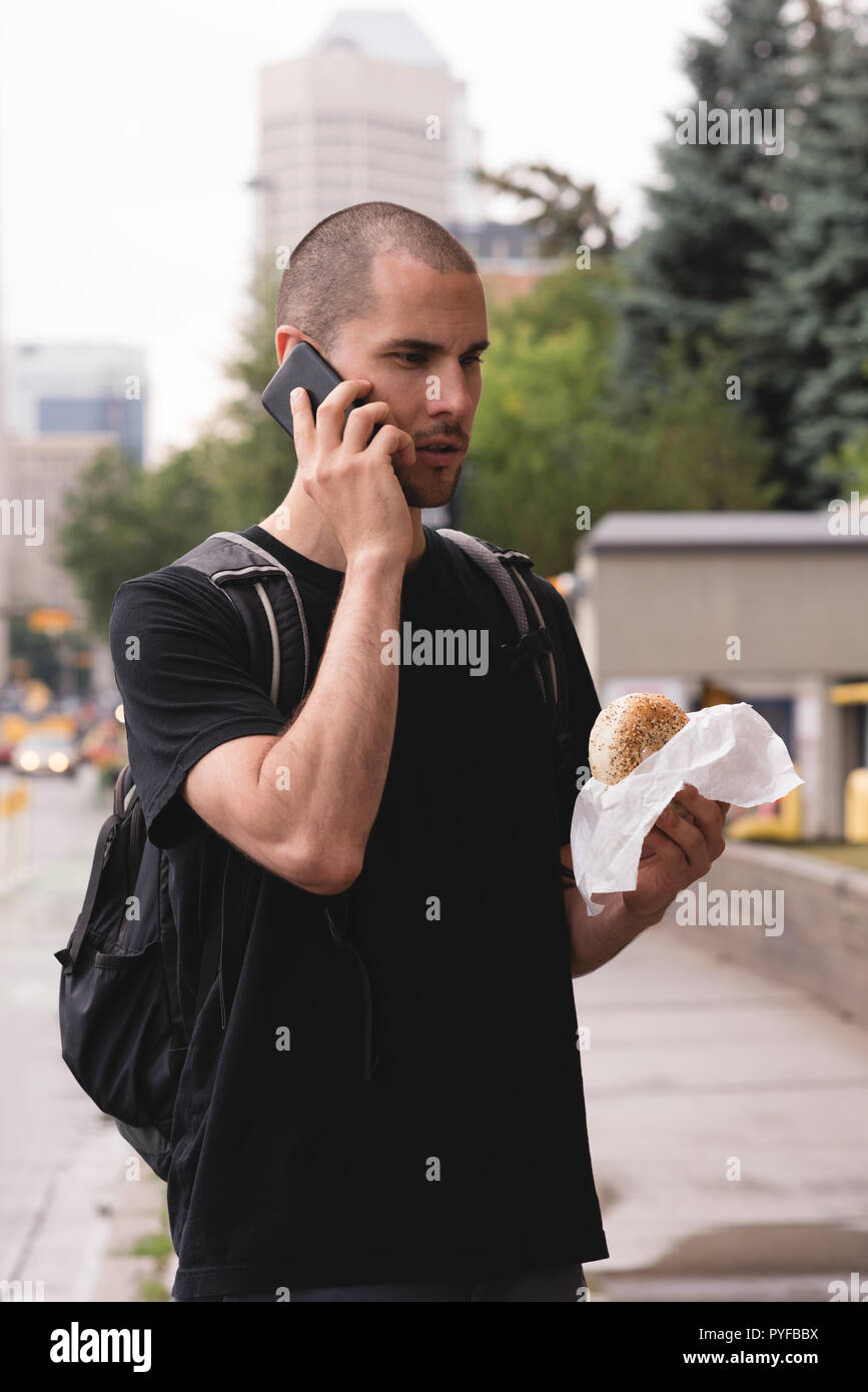 Junger Mann mit Burger auf dem Mobiltelefon Stockfoto