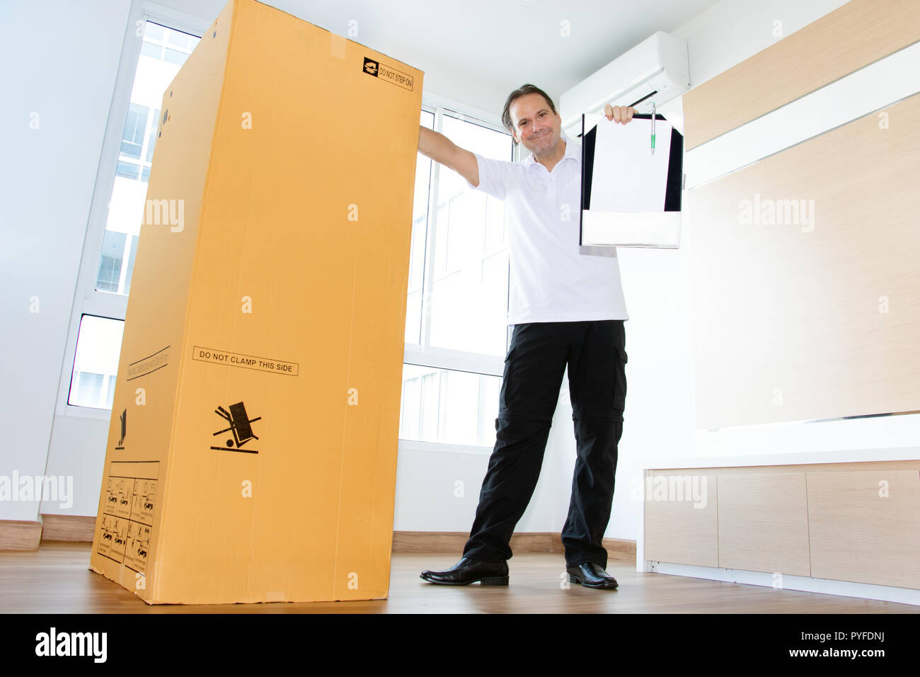 Ein Mann in einem leeren Raum zeigt ein leeres Papier für den Versand  großes Paket. Der Postbote liefert das Paket in die neue Wohnung  Stockfotografie - Alamy