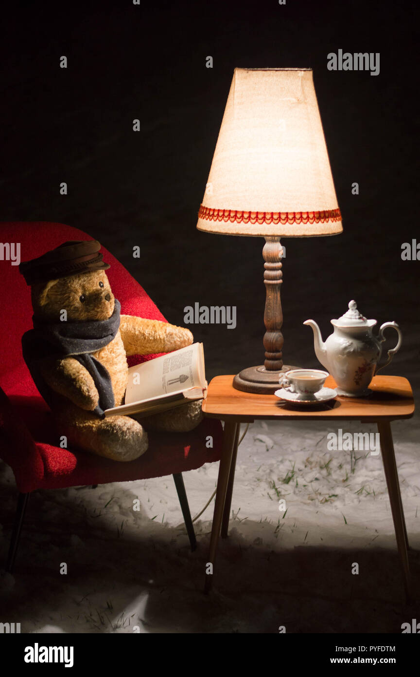 Surreale Szene mit einem Teddybär - im Garten im Winter ein kleines Wohnzimmer - rot Stuhl, Tisch, Lampe und Kaffee Service Set - warten auf Santa C Stockfoto