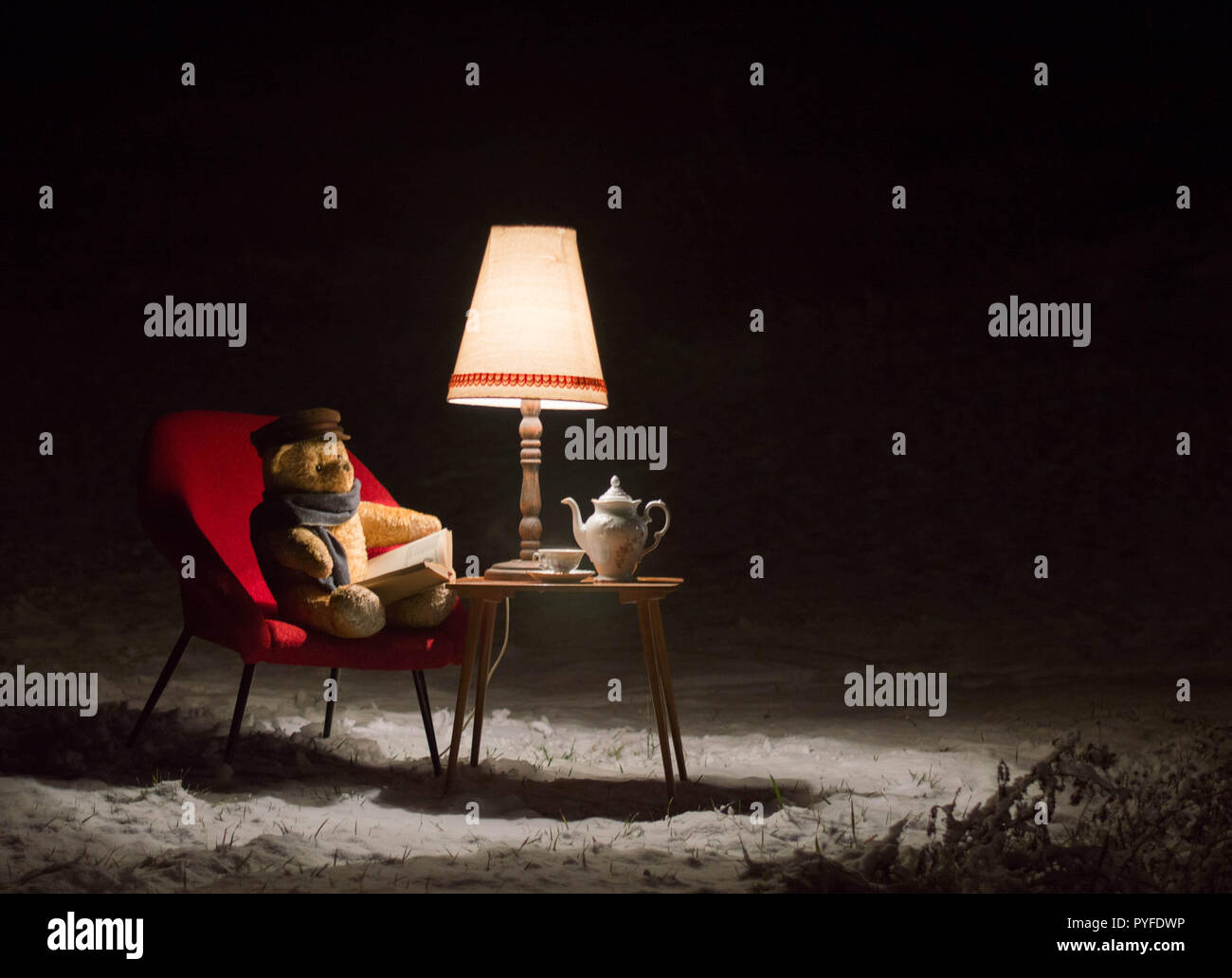 Surreale Szene mit einem Teddybär - im Garten im Winter ein kleines Wohnzimmer - rot Stuhl, Tisch, Lampe und Kaffee Service Set - warten auf Santa C Stockfoto