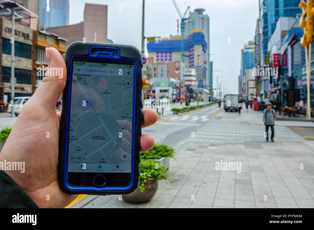 Eine männliche Hand mit einem Smartphone, die Verwendung von Google Maps um Haeundae, Teil von Busan in Südkorea zu navigieren. Stockfoto
