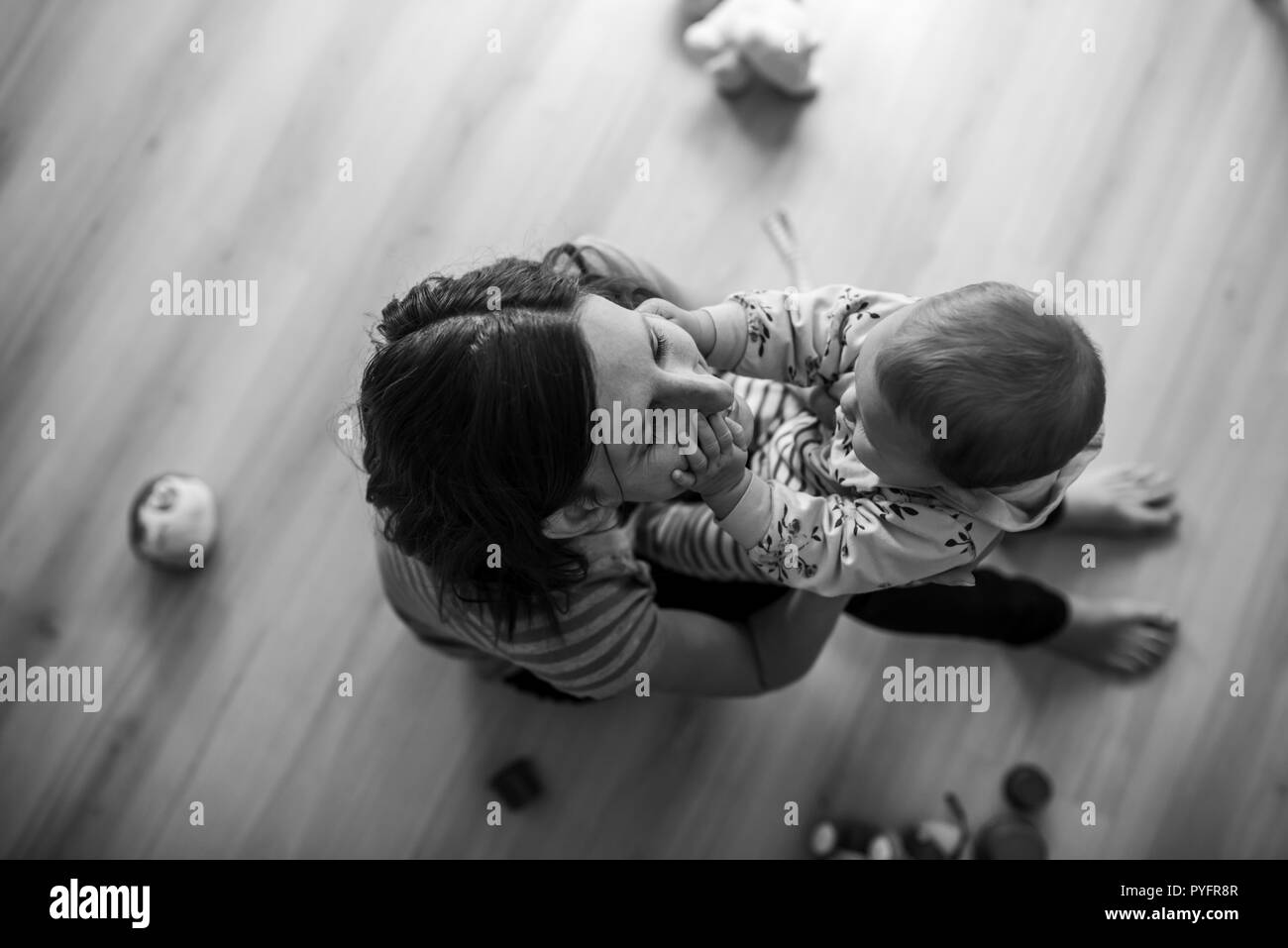 Blick von oben auf die junge Mutter sitzen im Wohnzimmer, liebevoll mit ihr spielen baby Tochter. Schwarzweißbild. Stockfoto