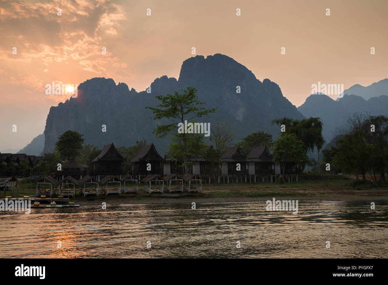 Leere Waterfront Restaurant und Bungalows durch den Nam Song Fluss und die Silhouette von Kalkstein Berge in Vang Vieng, Laos, bei Sonnenuntergang. Stockfoto