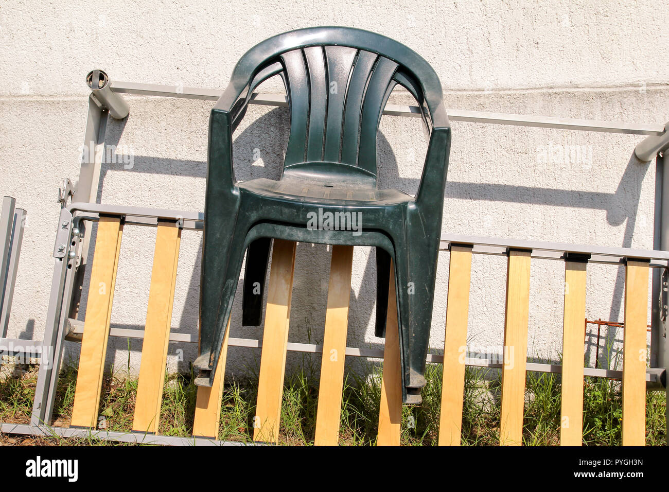 Grüne Plastikgartenstühle weggeworfen und auf einer Leiter, die von der  Wand in den Garten verlassen. Wand Hintergrund, Natur, Stuhl Möbel.  Recycling Industrie Stockfotografie - Alamy