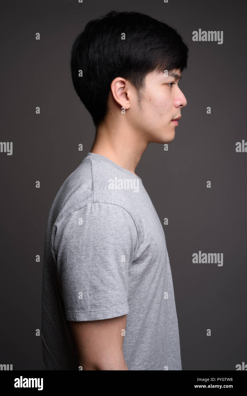 Profil anzeigen von jungen Hübschen asiatischen Menschen gegen den grauen Hintergrund Stockfoto