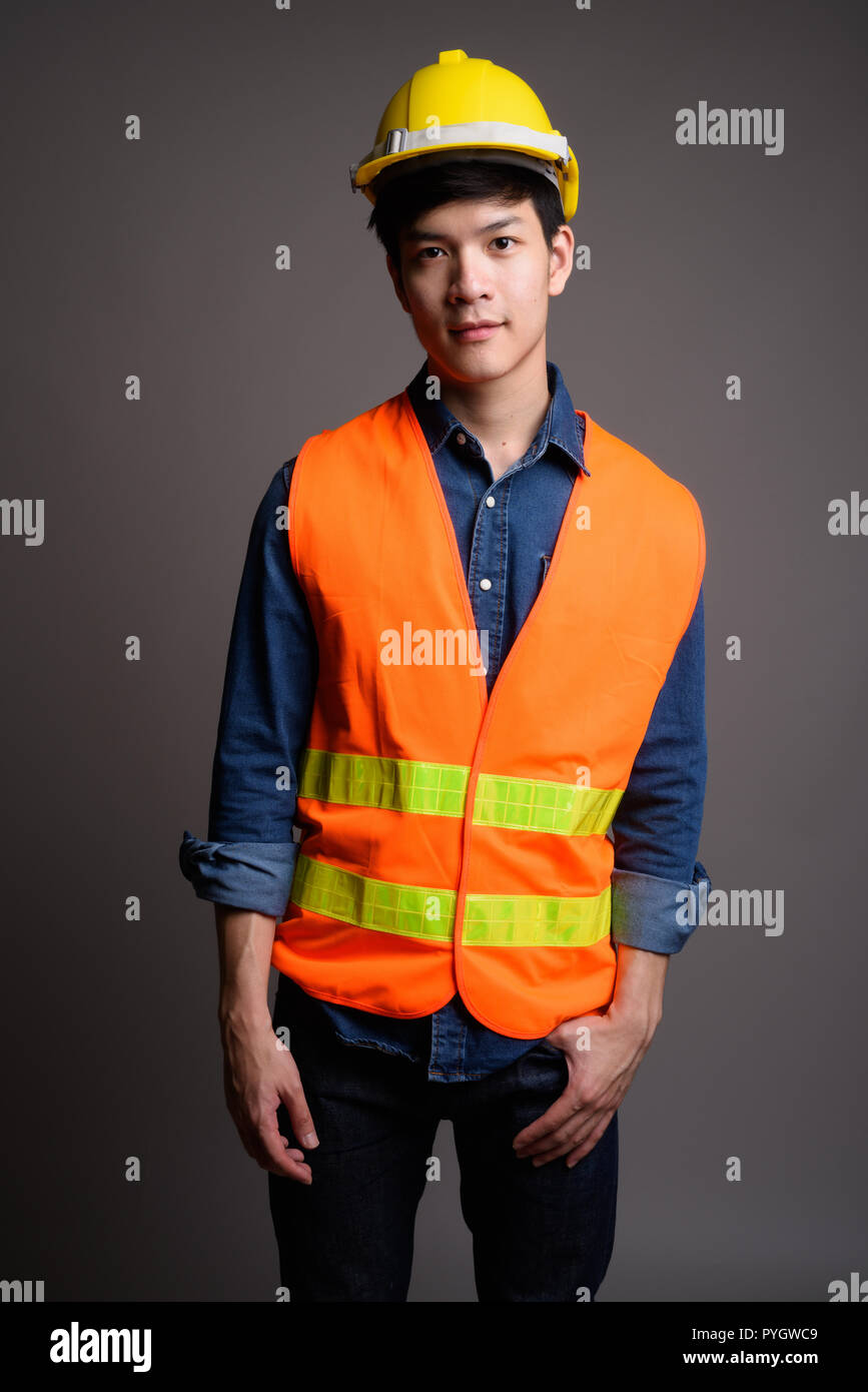 Die Jungen gut aussehenden asiatischer Mann Bauarbeiter gegen Grau backgr Stockfoto