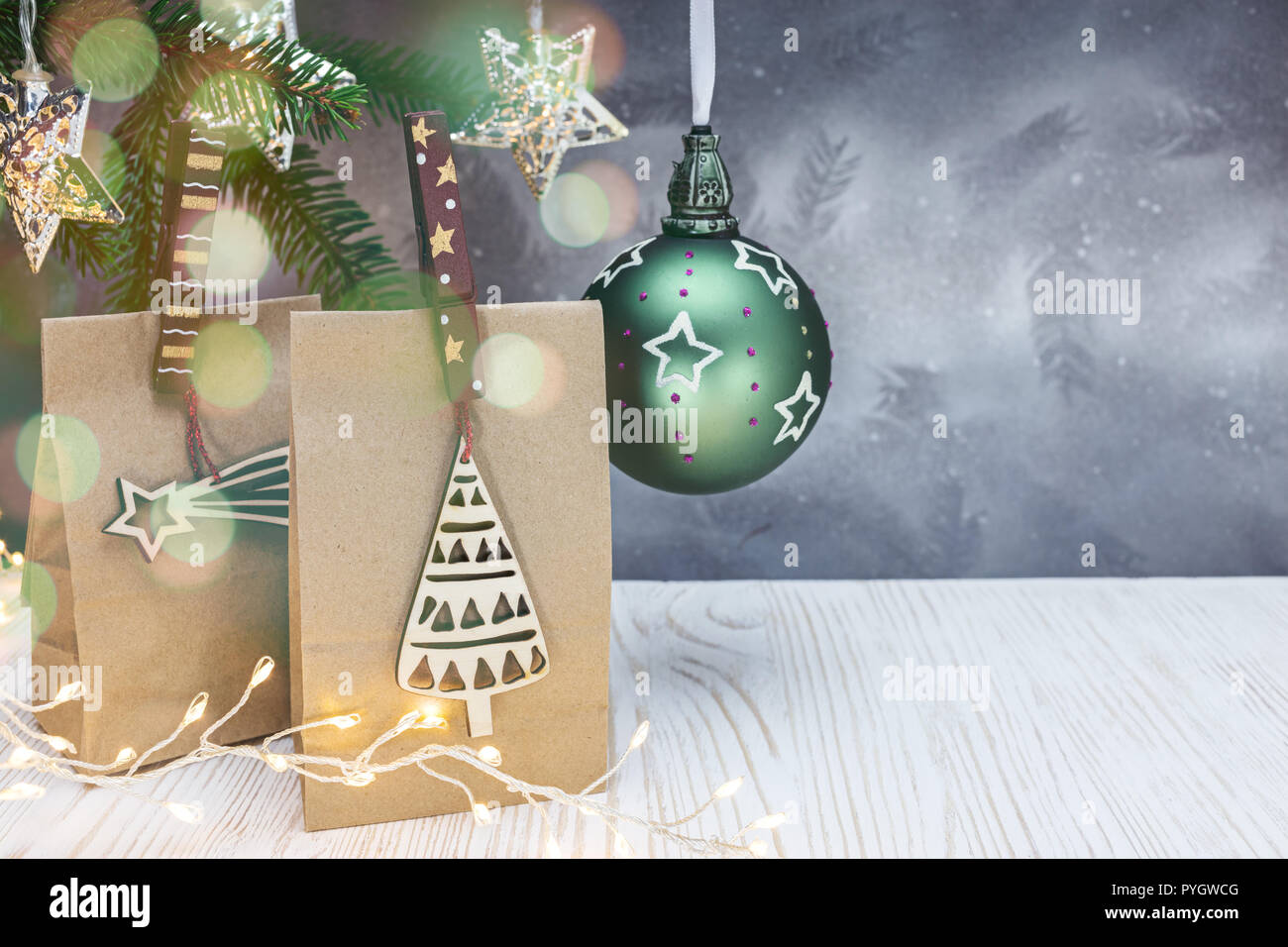 Papier Geschenkbeutel mit hölzernen Stiften eingerichtet, christmas ball, Fir Tree Branch und leuchtende Lichter an Weihnachten Hintergrund Stockfoto
