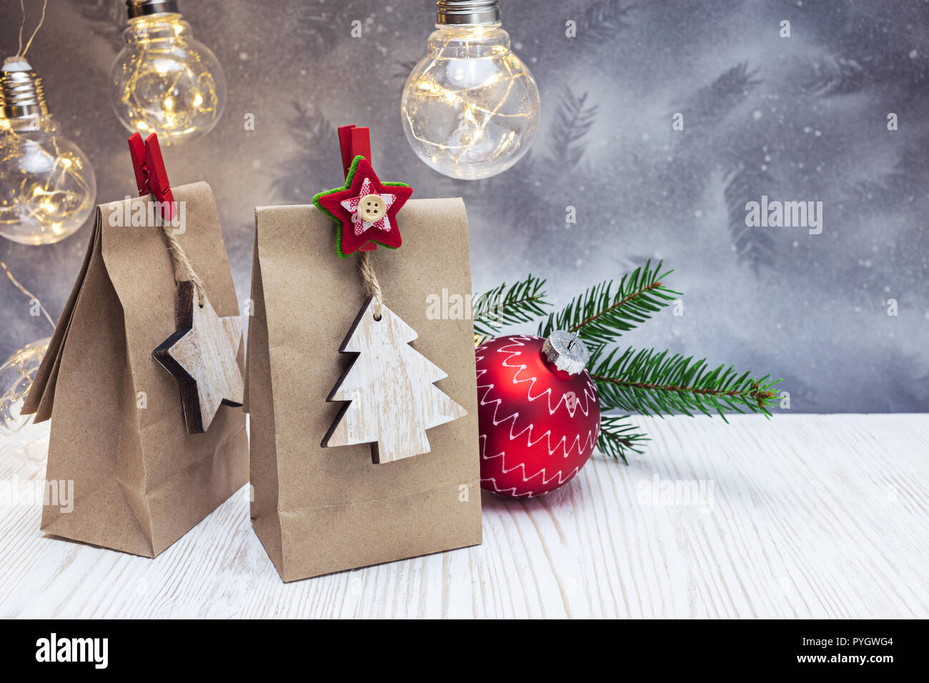 Papier Geschenkbeutel und rote dekorative Kugel mit retro Licht Lampen und Grüne Tanne Baum gegen festliche Weihnachten Hintergrund Stockfoto